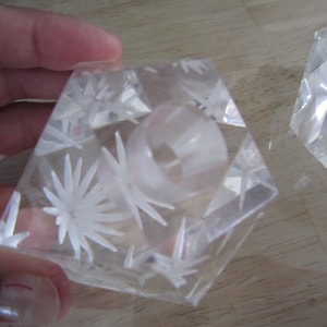 May include: Two clear glass candle holders with a starburst design. The candle holders are shaped like a pyramid with a square base.
