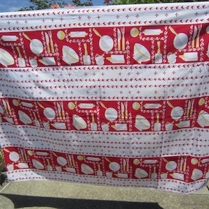 May include: Red and white tablecloth with a repeating pattern of kitchen utensils, bowls, and rolling pins. The pattern is outlined in yellow.