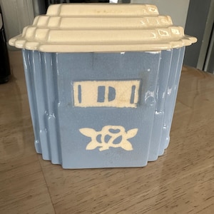 May include: A vintage blue and cream ceramic cookie jar. The jar has a rectangular shape with a stepped lid and a floral design. The jar has a rectangular shape with a stepped lid and a floral design.