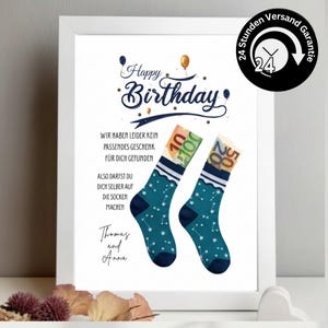 Pode incluir: Uma impressão de aniversário emoldurada com o texto Happy Birthday e frases em alemão, apresentando duas meias azul-petróleo com padrão de estrelas brancas. Cada meia contém notas de euro enroladas. A impressão inclui os nomes Thomas e Anna.