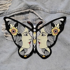 Könnte beinhalten: Schwarzer und weißer gestickter Schmetterlings-Patch mit zwei weiblichen Gesichtern und gelben Blumen. Der Patch befindet sich auf einem hellblauen Jeans-Hintergrund.