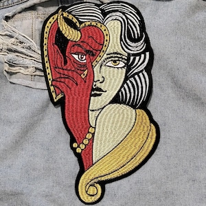 May include: Embroidered iron-on patch featuring a woman with a devil's face behind her, with red, gold, and white thread details.