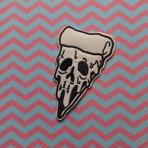 May include: A white fabric patch with a black outline of a pizza slice with a skull face. The pizza slice is dripping with cheese.