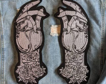 Könnte beinhalten: Zwei schwarze Bügeleisen-Patches mit einem silbernen gestickten Design von Händen mit Rosen. Die Hände sind in einer Gebetsposition mit ineinander verschlungenen Fingern. Die Rosen befinden sich am unteren Ende der Hände.