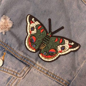 May include: A blue denim jacket with a colourful embroidered butterfly patch. The butterfly has red, white, blue, green, and black accents.
