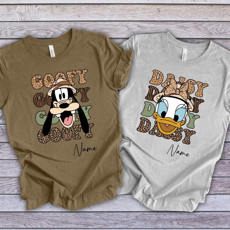 May include: Two brown and grey t-shirts with a safari theme. The brown shirt features Goofy with the text "Goofy Goofy Goofy Goofy" and the grey shirt features Daisy Duck with the text "Daisy Daisy Daisy Daisy".