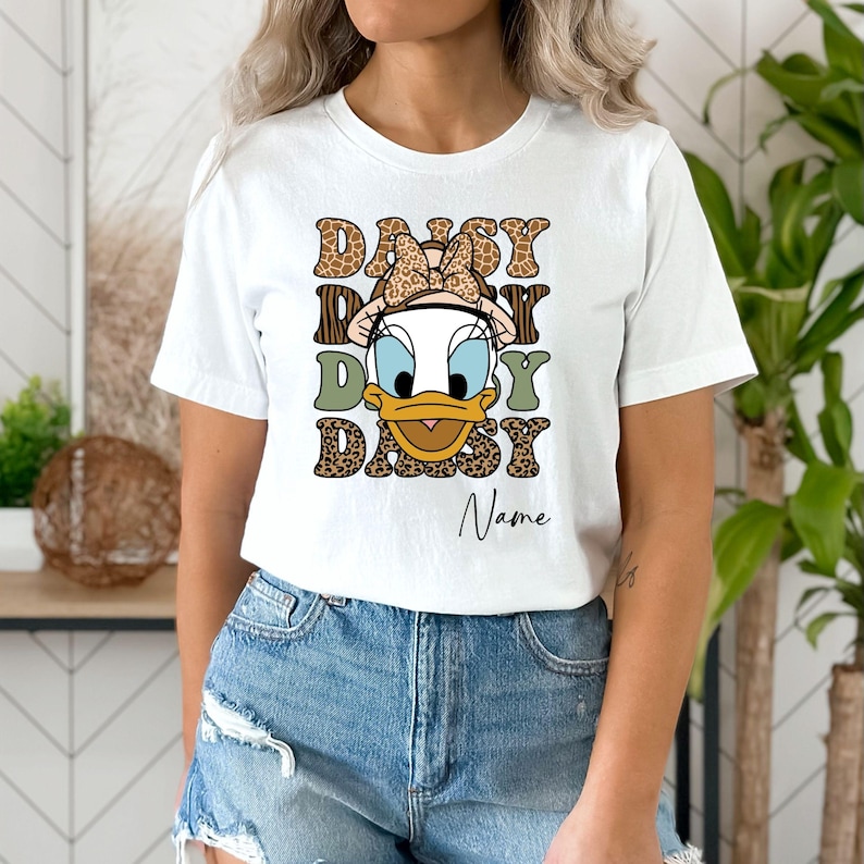 May include: White t-shirt with a cartoon duck wearing a bow and a leopard print design. The text "Daisy Daisy Daisy" is printed on the shirt with the name "Name" below it.
