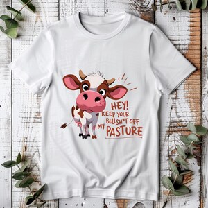 May include: White t-shirt featuring a cartoon cow and the text "Hey! Keep your bullsh*t off my pasture".