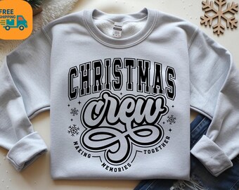 May include: A pale grey sweatshirt featuring the text "CHRISTMAS CREW" in a black, bold, collegiate-style font. The word "crew" is in a cursive font. The phrase "MAKING MEMORIES TOGETHER" is below the word "crew". Snowflakes are also included.