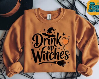 May include: An orange sweatshirt with the phrase "Drink up Witches" in black script, featuring a witch hat, wine glass, and broom. The design is perfect for Halloween or a witch-themed event.