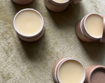 May include: Multiple small, round, cardboard containers with lids. Each container holds a pale yellow, waxy substance.
