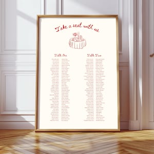 May include: A white wedding seating chart with a gold frame. The chart has a red illustration of a table with flowers and food. The text "Take a seat with us" is at the top of the chart. The chart lists the names of guests at two tables, "Table One" and "Table Two".