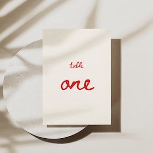 May include: White card with the text "table one" in red cursive writing.