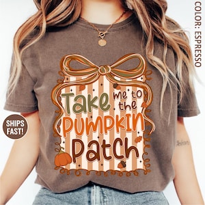 May include: Espresso-colored t-shirt featuring a fall-themed graphic. The design includes the text "Take me to the Pumpkin Patch" in orange and green, with a pumpkin, leaves, and acorns. The graphic is framed by a decorative border with a bow.
