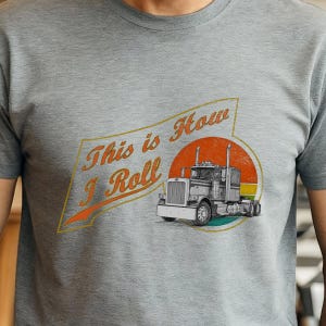 May include: A grey t-shirt with a graphic of a semi-truck and the text "This is How I Roll" in orange and yellow. The truck is detailed in black and white, set against an orange and yellow circle.