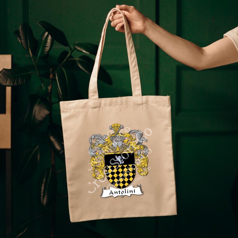 May include: A beige tote bag with a black and yellow coat of arms featuring the name "Antolini" printed on a white banner.