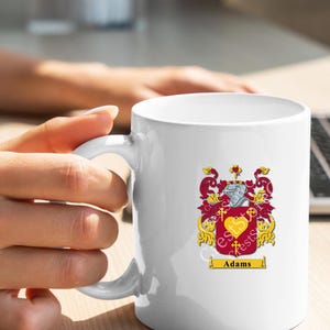 May include: White ceramic mug with a gold and red coat of arms design and the name "Adams" printed below.