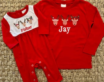 May include: Red long-sleeve shirts with embroidered reindeer and personalized names. The shirt on the left is a onesie with the name "Fisher" and the shirt on the right has the name "Jay".