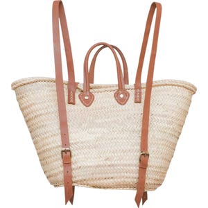May include: A natural woven straw tote bag with brown leather straps and buckles. The bag has two top handles and a zipper closure.
