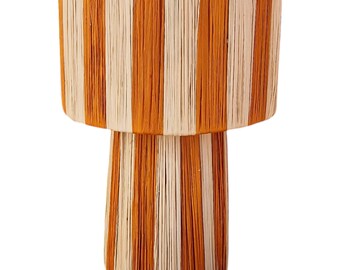 May include: A two-tiered table lamp with a striped design. The lamp is made of woven natural fibers and has a warm orange and cream color scheme.