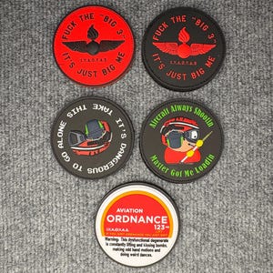 Puede incluir: Una colección de cinco parches redondos con varios diseños y texto. Los parches presentan frases como "FUCK THE BIG 3" y "Aircraft Always Shootin". Un parche dice "AVIATION ORDNANCE" con un mensaje de advertencia.