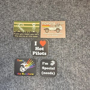 Puede incluir: Una colección de pegatinas cuadradas y rectangulares con varios diseños y texto. Una pegatina presenta un esqueleto y el texto "Fuck you mean you left the percs at the base." Otra dice "TOYOTA HILUX FOR REGIME CHANGES ON A BUDGET."