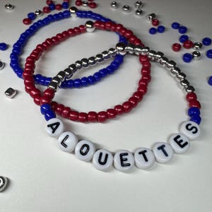 Peut inclure: Trois bracelets de perles rouges, blanches et bleues. L'un des bracelets épelle "ALOUETTES" avec des perles de lettres blanches. Les bracelets sont faits de petites perles rondes et de perles d'accent argentées.
