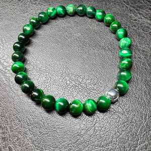 Puede incluir: Un brazalete de cuentas de ojo de tigre verde con cierre magnético plateado.