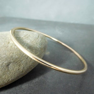 May include: A simple gold bangle bracelet. The bracelet is made of a smooth, round wire and is a classic, minimalist style.