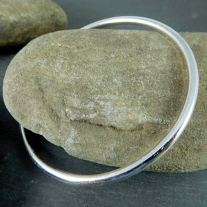 May include: A simple silver bangle bracelet, shown on a textured gray rock.