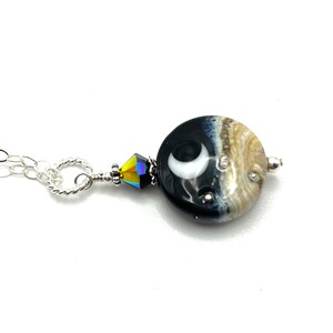 May include: A silver chain necklace with a black and white glass pendant featuring a crescent moon design. The pendant is accented with a clear crystal bead.