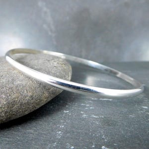 May include: A simple silver bangle bracelet, smooth and polished, resting on a gray stone.