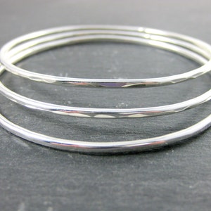 May include: Three silver bangles stacked on top of each other. The bangles are smooth and shiny.