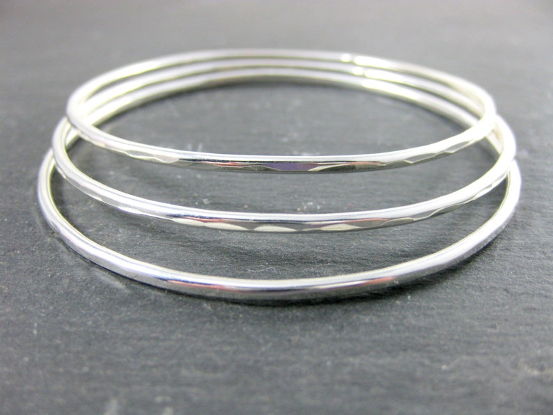 May include: Three silver bangles stacked on top of each other. The bangles are smooth and shiny.