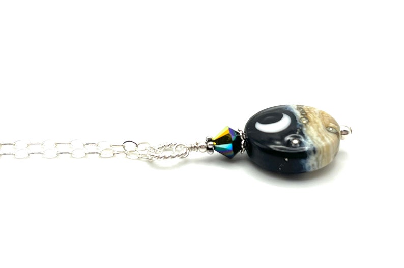 May include: A silver chain necklace with a black and white glass bead pendant featuring a crescent moon and stars. The bead is accented with a iridescent crystal.