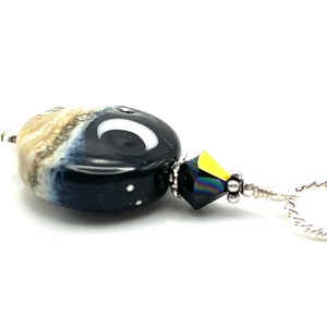 May include: A black and white glass bead with a crescent moon design, a black crystal bead, and a silver chain.