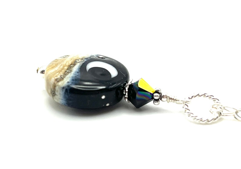 May include: A black and white glass bead with a crescent moon design, a black crystal bead, and a silver chain.