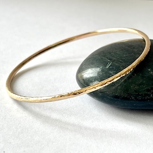 May include: A gold hammered bangle bracelet. The bracelet is simple and elegant, with a smooth, hammered finish.