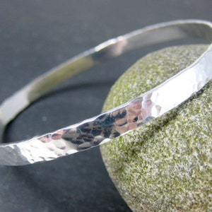 May include: A silver hammered bangle bracelet. The bracelet is smooth and shiny, with a hammered texture.