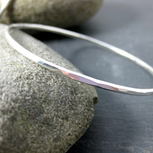 May include: A silver hammered bangle bracelet. The bracelet is thin and has a smooth, polished finish.