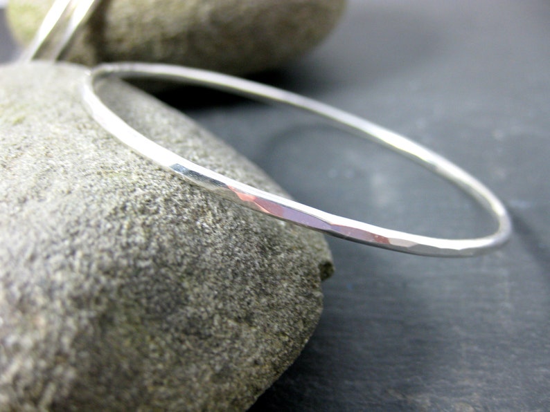 May include: A silver hammered bangle bracelet. The bracelet is thin and has a smooth, polished finish.