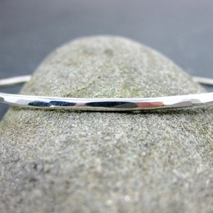 May include: A silver hammered bangle bracelet. The bracelet is thin and delicate, with a smooth, polished finish.
