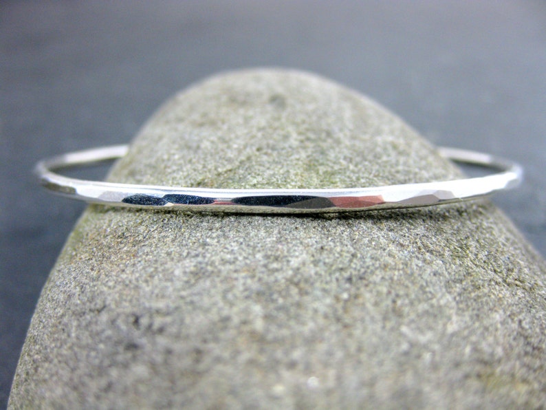 May include: A silver hammered bangle bracelet. The bracelet is thin and delicate, with a smooth, polished finish.