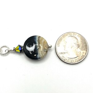 May include: A silver chain necklace with a black and white glass bead featuring a crescent moon design. The bead is accented with a clear crystal. The necklace is shown next to a US quarter for size comparison.