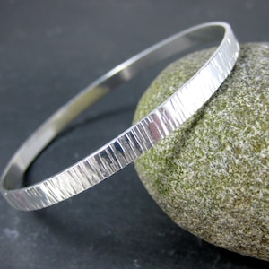 May include: A silver bangle bracelet with a textured, hammered finish. The bracelet is simple and elegant, and would make a great gift.