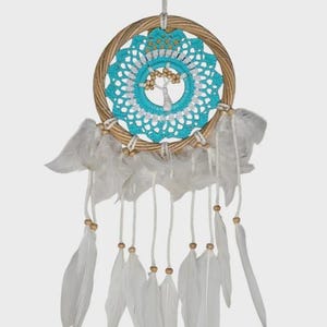 Peut inclure: Un attrape-rêves artisanal avec un anneau en rotin tressé, un centre crocheté turquoise et blanc avec un motif d'arbre et des plumes blanches suspendues en dessous. Des perles en bois ornent le design. Une décoration murale.