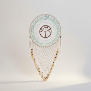May include: A handcrafted dreamcatcher with a white, mint green, and brown color scheme. The circular design features a tree of life in the center, surrounded by intricate macrame and beaded accents. Tassels hang from the bottom.