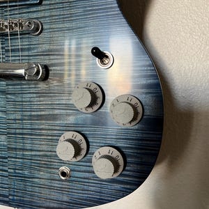 May include: Close-up of a blue electric guitar with chrome hardware and four knobs. The knobs are numbered 1-11.