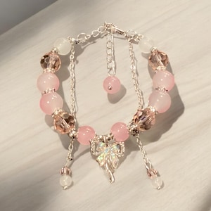 May include: A pink and silver bracelet with a bow charm. The bracelet is made with pink and clear beads and a silver chain.