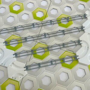 Könnte beinhalten: Nahaufnahme eines modularen Bausatzes mit Wabenmuster. Das Set besteht aus grauen, weißen und lindgrünen sechseckigen Fliesen sowie grauen Schienenteilen. Die Fliesen haben weiße Zentren und die Schienenteile sind über den Fliesen angeordnet.